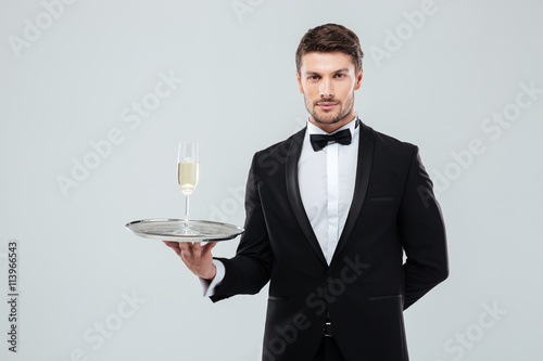 Butler in tuxedo holding tray with glass of champagne