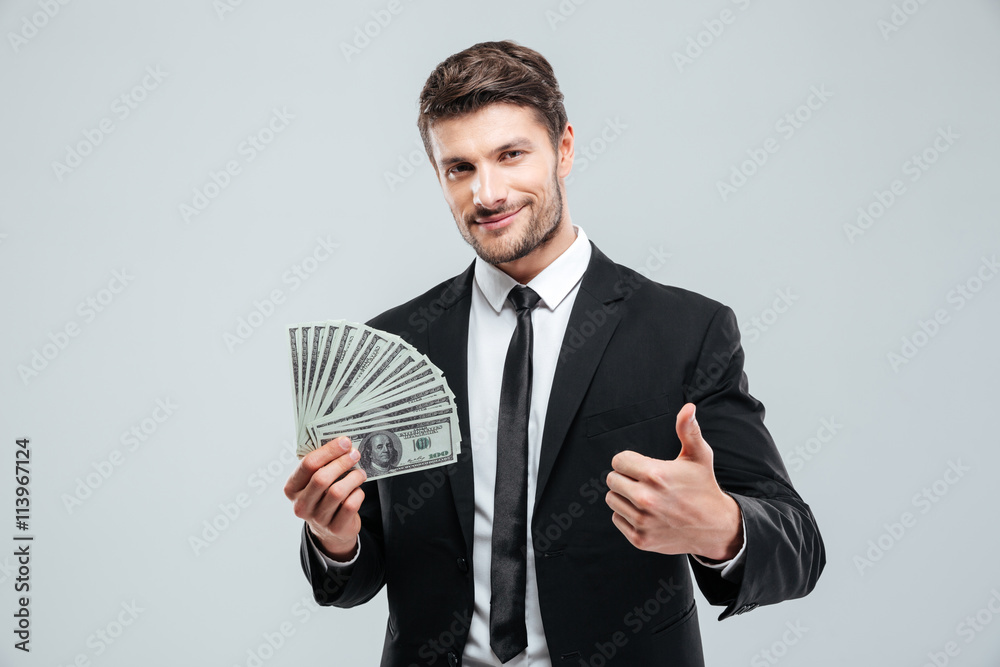 Smiling young businessman holding money and showing thumbs up Smiling young businessman holding money and showing thumbs up