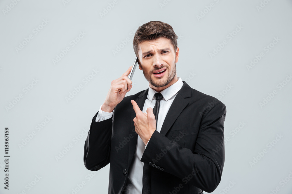 Confused young businessman talking on cell phone Confused young businessman talking on cell phone