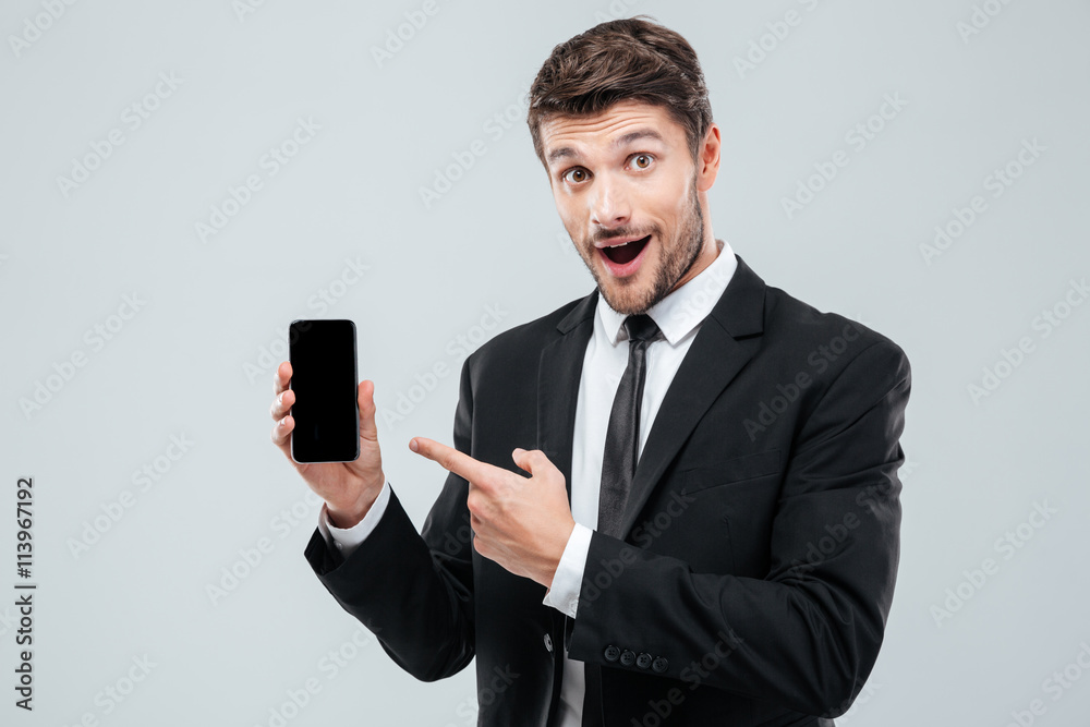 Amazed young businessman holding and pointing on blank screen smartphone Amazed young businessman holding and pointing on blank screen smartphone