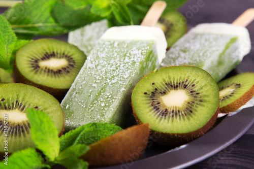 Homemade kiwi popsicles on a plate with mint and kiwi slices on a dark wooden background