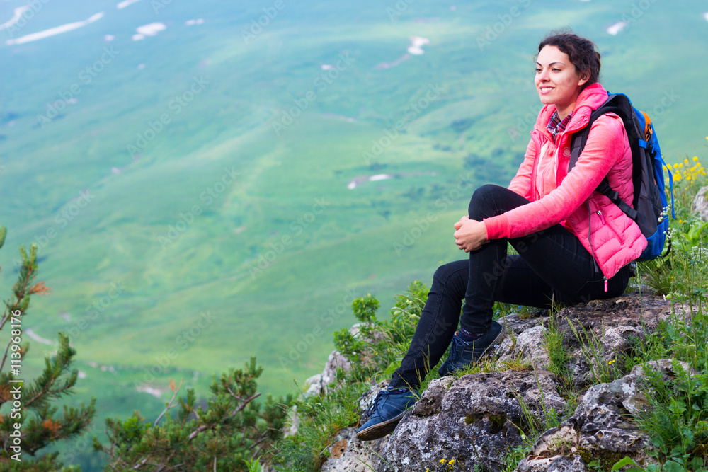 Woman Hiker with backpack relaxing on top of a mountain and look