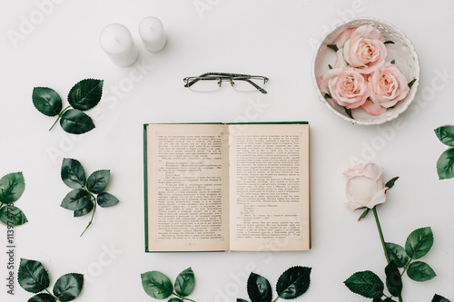 Opened book, glasses, pink roses on white background. Flat Lay