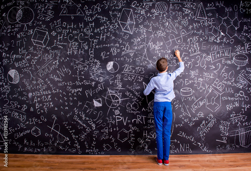 Boy against big blackboard with mathematical symbols and formula