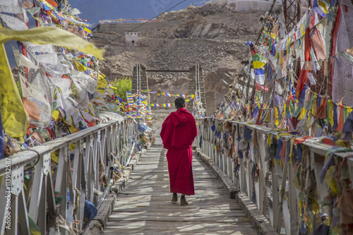 A monk walks onthe bridge pathway surrounded by colorful tibetan