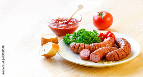 Roasted sausage with bread  herbs  sauce and tomatoes served on white plate and wood board