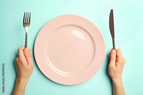 Fotografia Female hands with cutlery and empty plate on turquoise background
