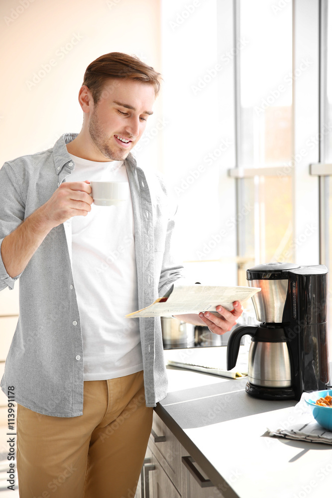 Young man making coffee and reading newspaper in kitchen Young man making coffee and reading newspaper in kitchen