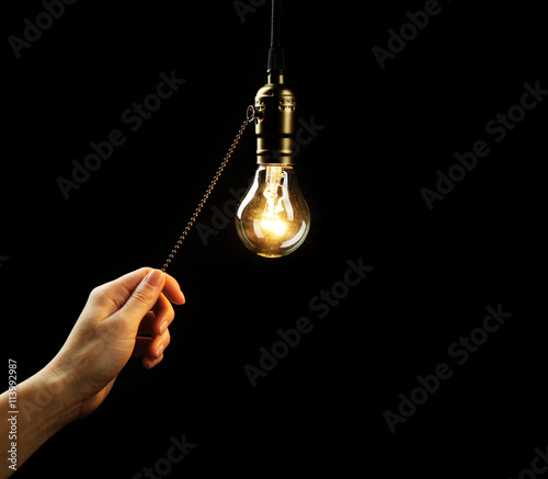 Female hand turning on light bulb on black background, close up