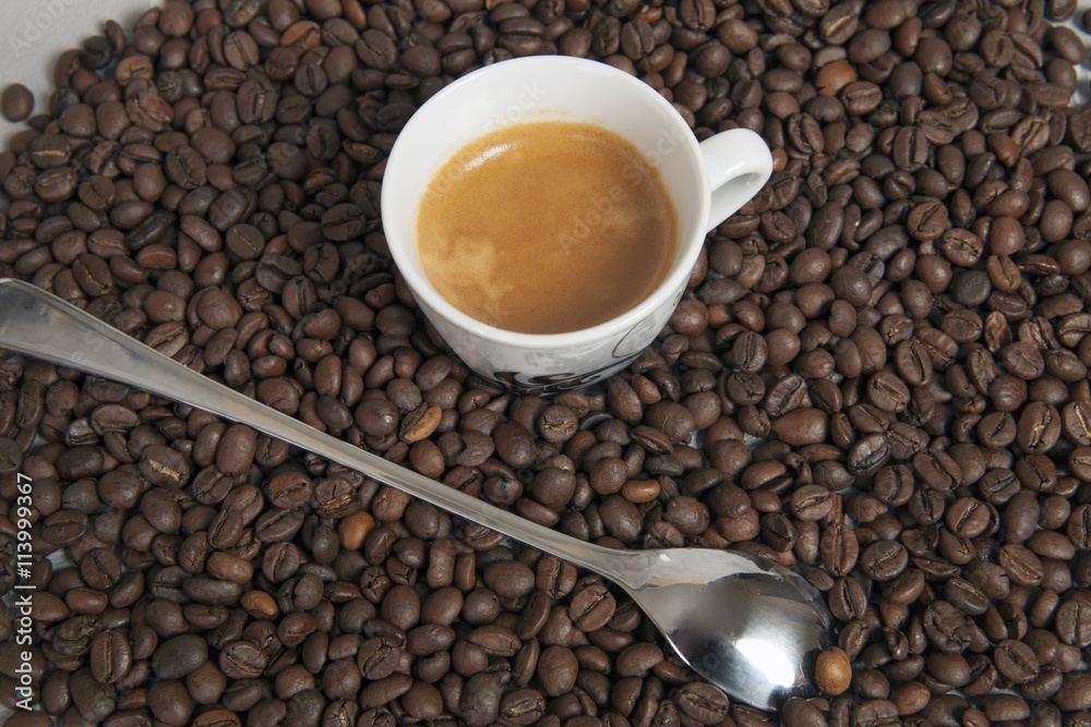 Naklejka premium Long spoon to coffee latte and fresh espresso cap. Background dark coffee beans