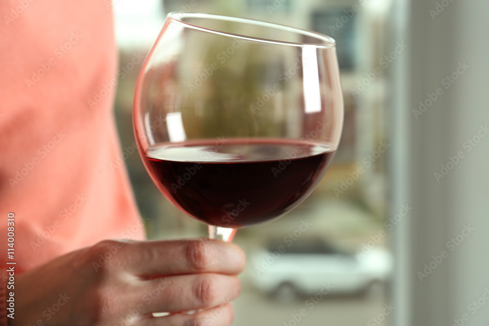 Female hand holding glass of red wine on blurred background