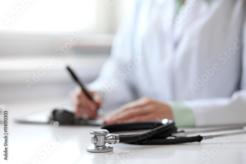 Close up of unknown female doctor sitting at the table near the window in hospital and typing at laptop computer