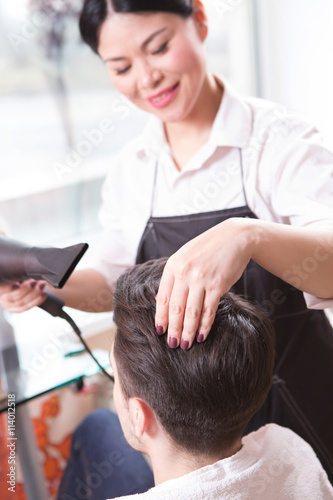 Picture of hair stylist or barber girl drying man's hair with hair dryer. Handsome man having his hair dried in hairdressing saloon.