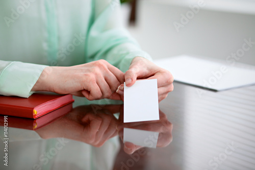 Business woman hands in a green blouse sitting at a desk in an office and holds out business card.