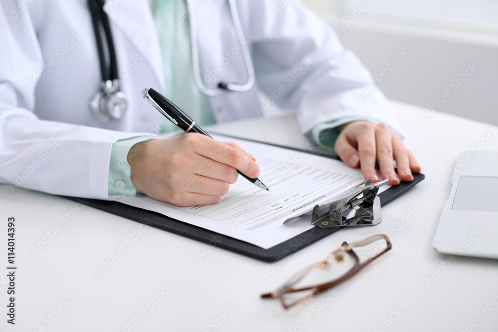 Close-up of a female doctor filling out application form , sitting at the table in the hospital Close-up of a female doctor filling out application form , sitting at the table in the hospital