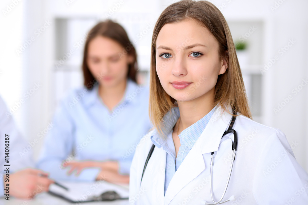 Young beautiful female doctor smiling on the background with patient and his doctor in hospital. High level and quality medical service concept. Young beautiful female doctor smiling on the background with patient and his doctor in hospital. High level and quality medical service concept.