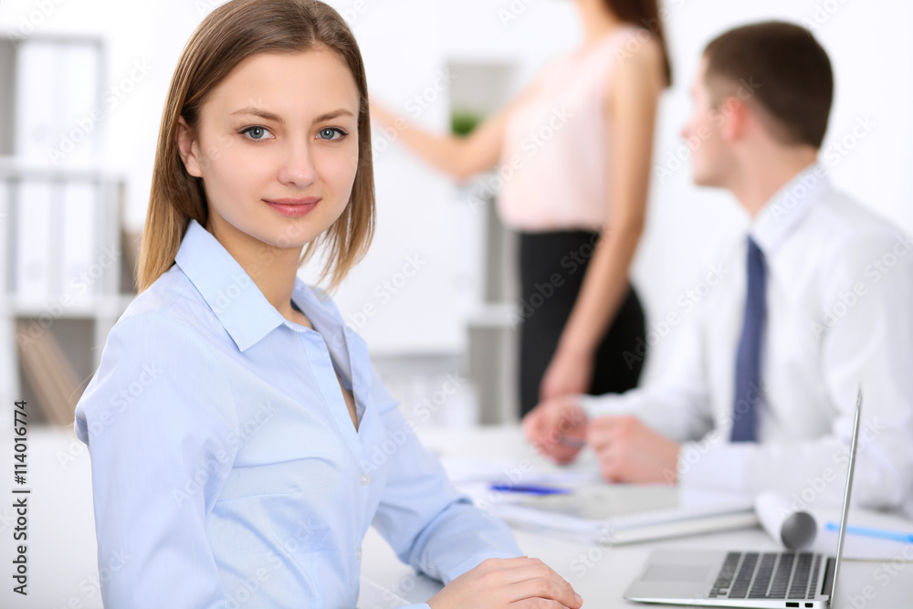 Fototapeta premium Portrait of a young business woman against a group of business people at a meeting.