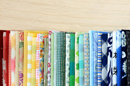Stack of multi-colored fabrics with different textures on wooden background.