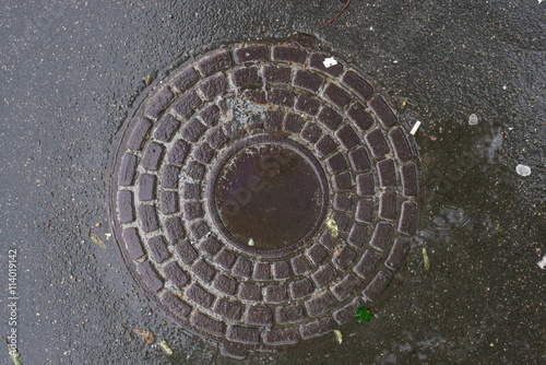 Closeup photo of Old Sewer rust manhole cover on the urban asphalt road. Rain scene.