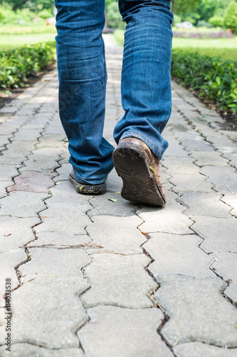 Man wearing jeans walking on the path to the park or garden