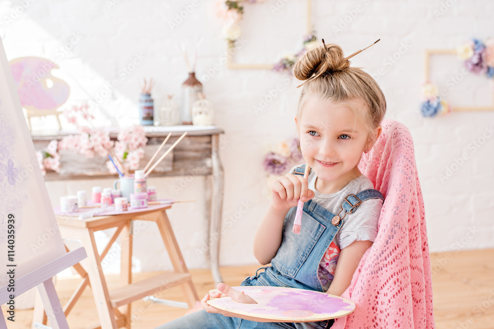 Little artist in denim overalls painting brushes on the easel in her studio Little artist in denim overalls painting brushes on the easel in her studio