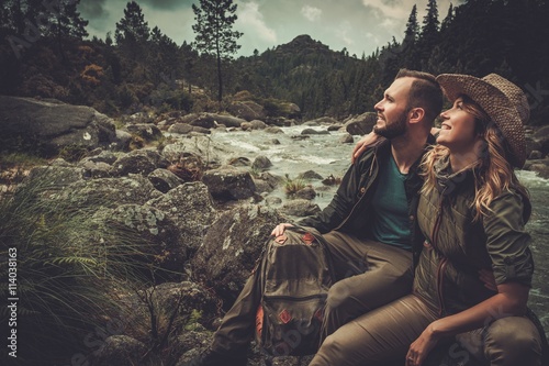 Cheerful couple hikers sitting near wild mountain river. photo