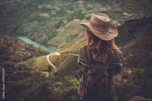 Woman hiker with backpack enjoying amazing valley landscapes on a top of mountain.