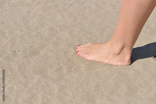 Woman feet with red pedicure walking on the hot sand of the beac © axentevlad