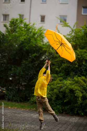 Little fellow in a bright yellow raincoat flies over the earth with an umbrella in hand.
