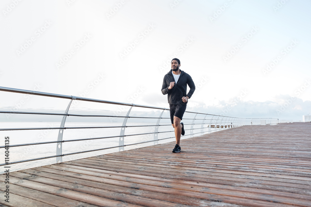 Concentrated african sportsman running on pier in the morning