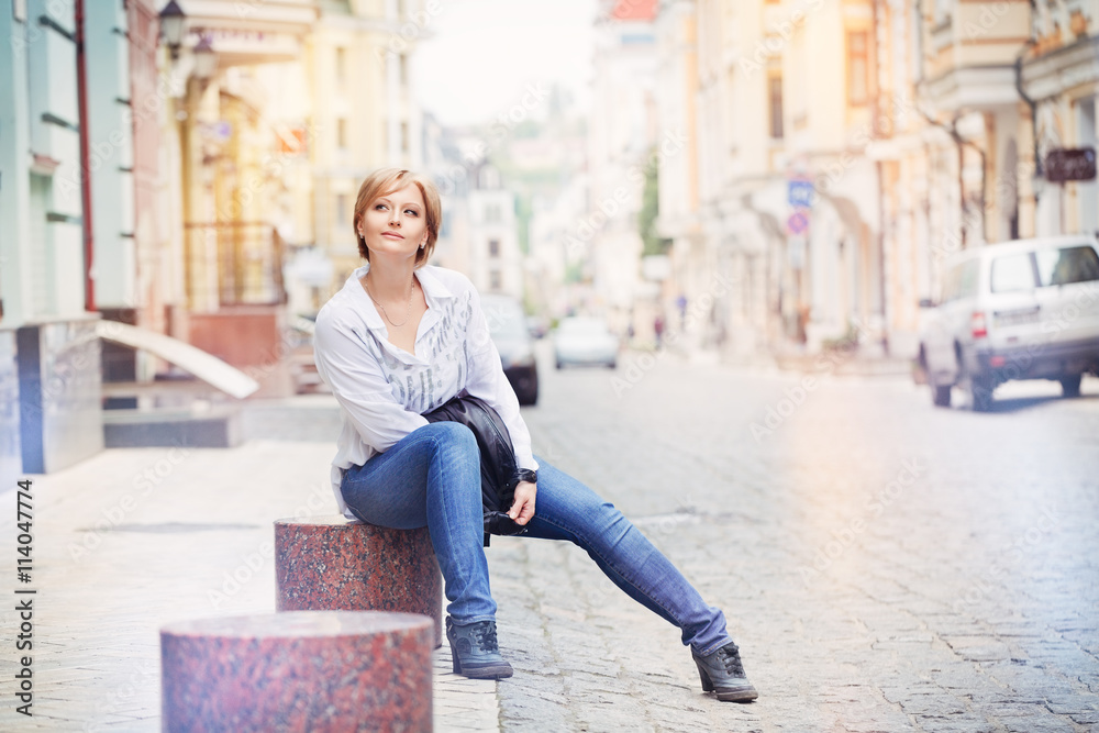 Young beautiful blond woman sitting on street at town.