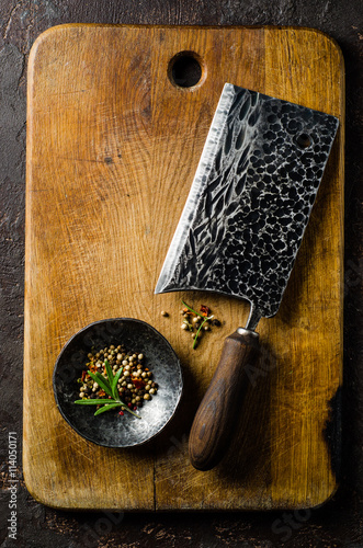 Chopping board block and Meat cleaver large chef's knife and bowl with spice on dark background. Vertical top view photo