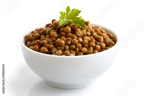 White ceramic bowl of brown cooked lentils with parsley isolated