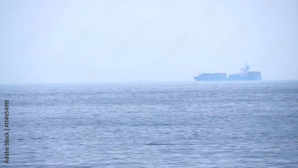 Cargo freighter ship sailing, moving at ocean horizon sky in hazy sea Cargo freighter ship sailing, moving at ocean horizon sky in hazy sea