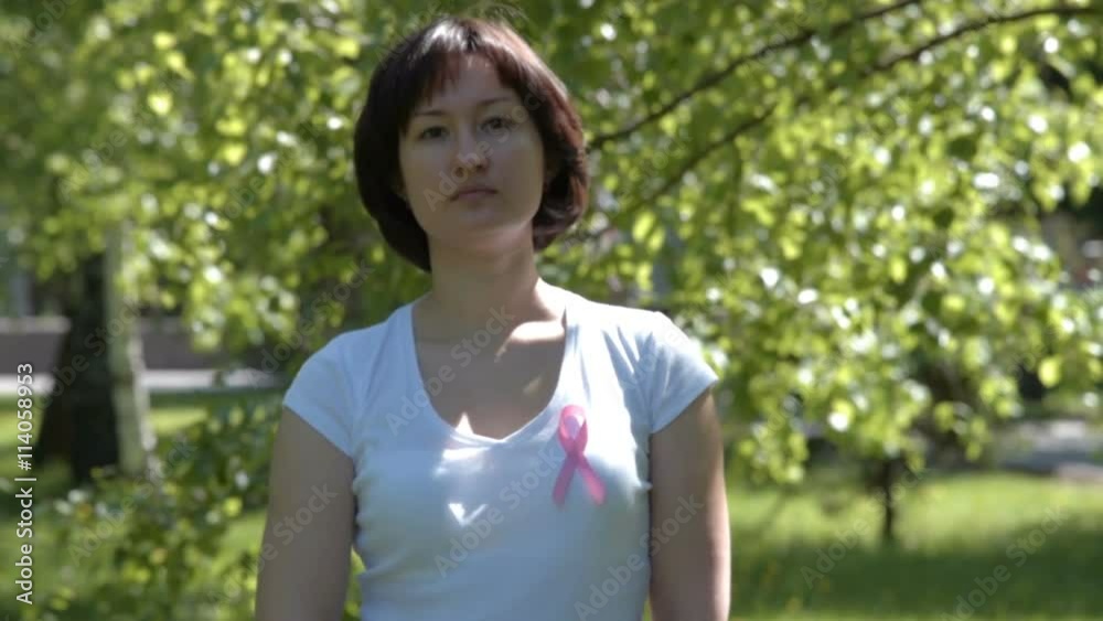 Woman pinning pink ribbon on white t-shirt, trees in background. Breast cancer awareness Woman pinning pink ribbon on white t-shirt, trees in background. Breast cancer awareness