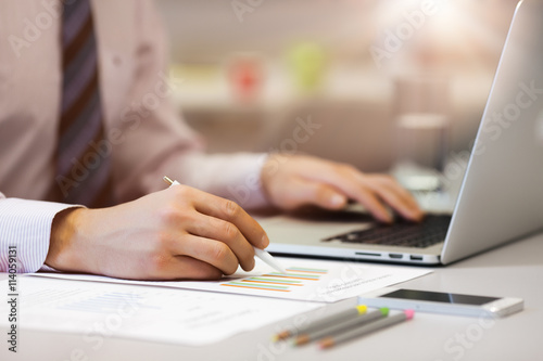 Business Person reading Data on paper Charts and Computer