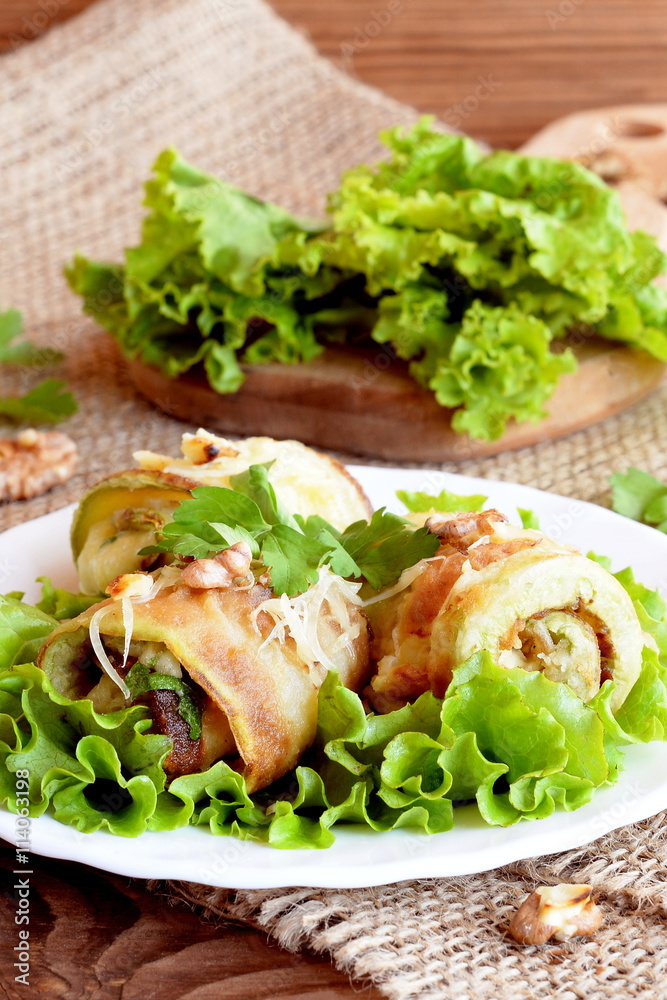 Fried zucchini rolls with cheese, walnuts and herbs. Fried stuffed zucchini rolls on a plate. Fresh lettuce leaves on a wooden board. Healthy and delicious summer appetizer Fried zucchini rolls with cheese, walnuts and herbs. Fried stuffed zucchini rolls on a plate. Fresh lettuce leaves on a wooden board. Healthy and delicious summer appetizer