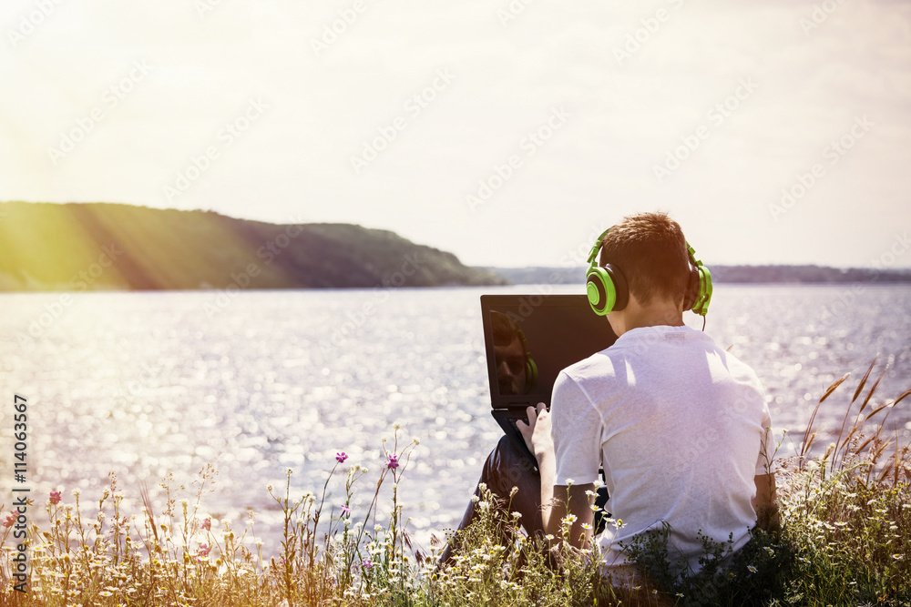 Fototapeta premium teenager working at the computer on the river bank