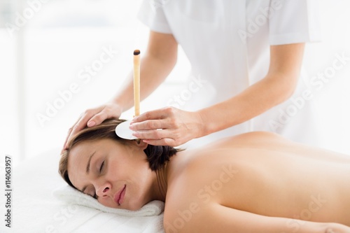 Woman receiving ear candle treatment from masseur photo