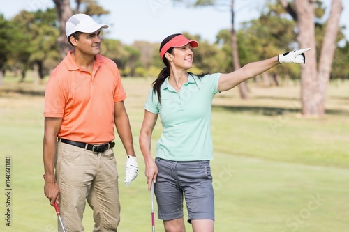 Happy golfer woman pointing while standing by man 