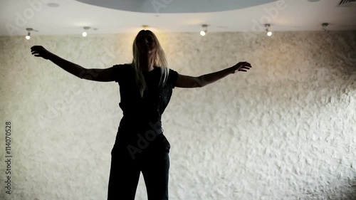 Young hip-hop and house female dancer dressed in black performing in the dancing hall. The dark silhouette of dancing girl in front of light wall photo