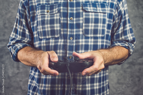 Gamer in plaid shirt playing video game with gamepad