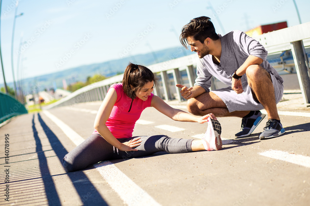 Young couple exercising and stretching muscles before jogging. Young man helps a young woman to stretch her legs.
