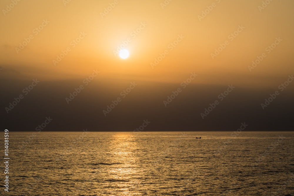 A golden stripe on the water during sunset at sea, silhouette of 2 people on a boat