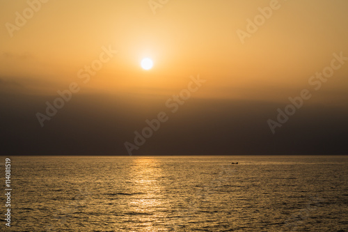 A golden stripe on the water during sunset at sea  silhouette of 2 people on a boat