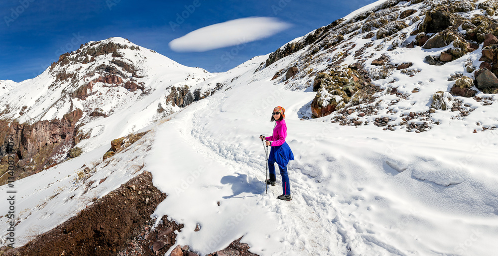 woman hiking on a snowy trail in the Caucasus mountains on the background of unusual lenticular cloud