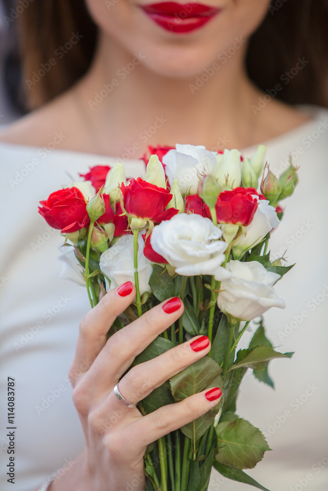 Close up of a bride holding a wedding bouquet with red and white roses.