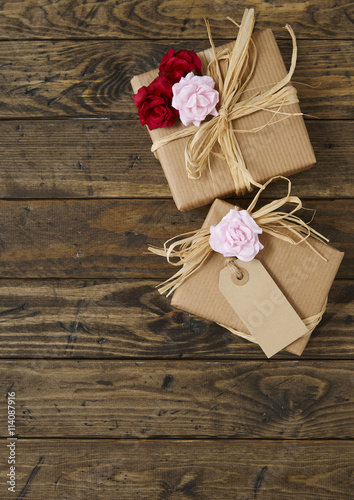 Gift wrap - Presents wrapped in brown parcel paper with raffia bows, blank tag, and red and pink roses on a rustic wooden table top background forming a page border