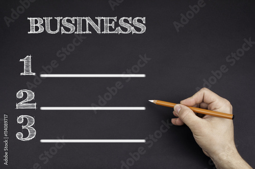 Hand with a white pencil writing: BUSINESS blank list