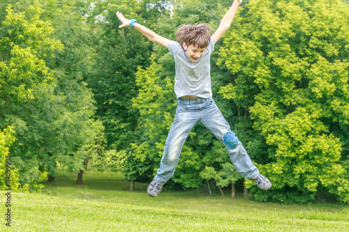 Adorable young child boy in the park. On warm summer day during school holidays. Kid boy jumping and smiling.
